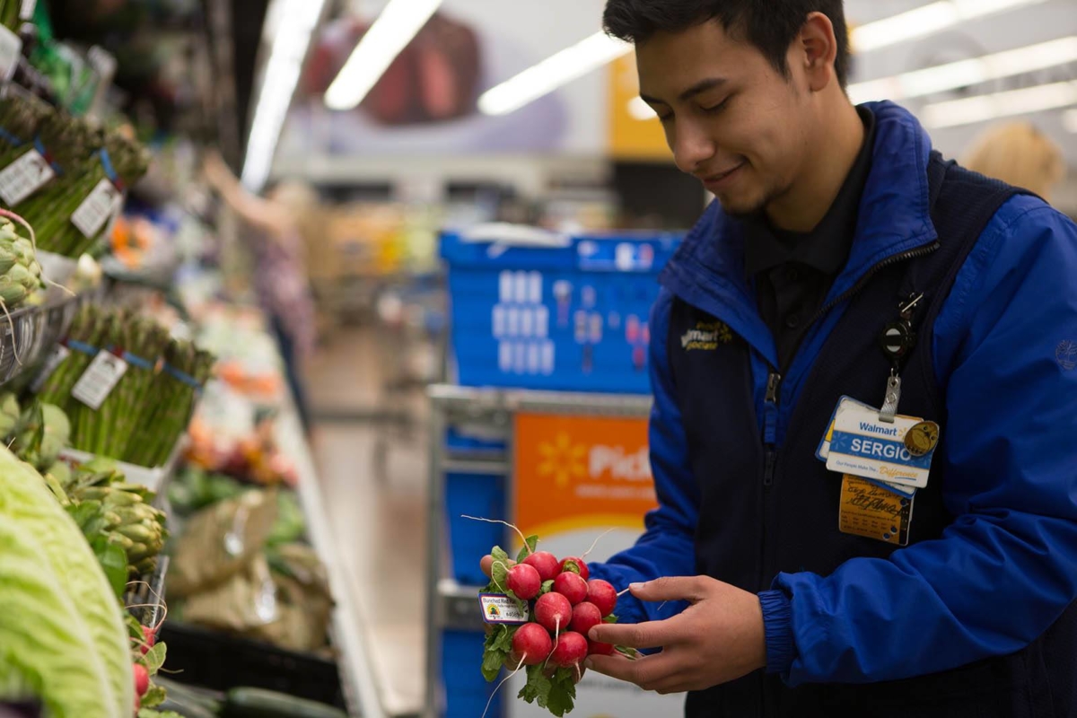 A male Hispanic Walmart employee picking up some radishes